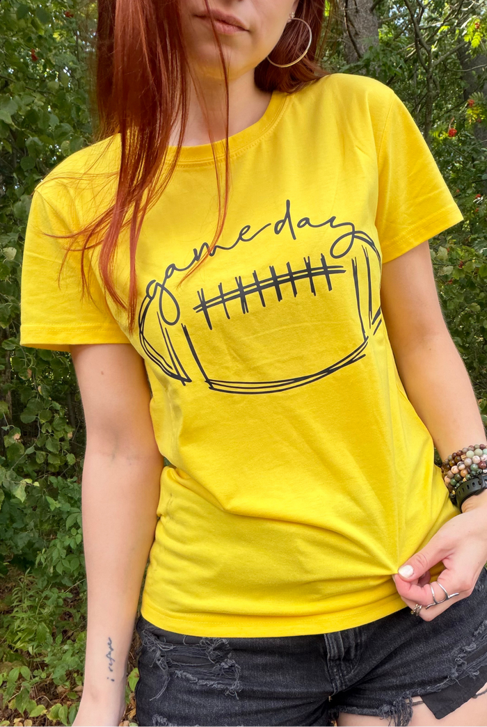 A woman wearing a bright yellow graphic t-shirt with a black football outline and the word 'gameday' written across the chest
